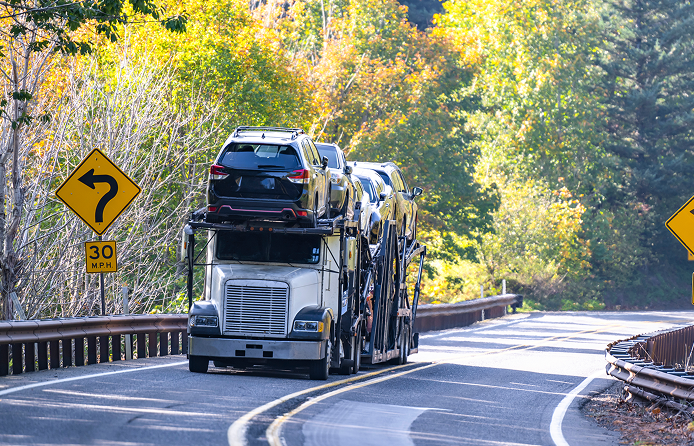 Truck transporting cars on a winding road.